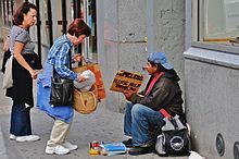 two people sitting on the side of a building talking to each other while another person stands next to them