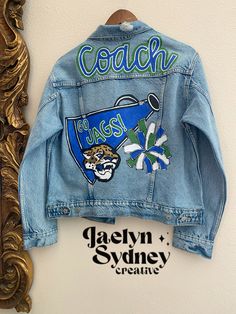 Sports Team Jean Jacket Diy, Cheer Coach Jean Jacket, Cheer Jean Jacket, Cheer Coach Outfit Style, Painted Jean Jacket School Spirit, Senior Jean Jacket, Bedazzled Jean Jacket, Letterman Jacket Ideas, Cheer Banners