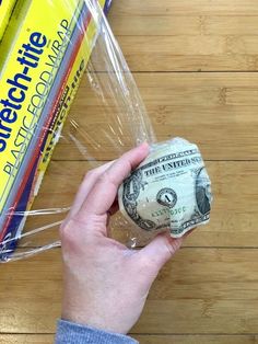 a person holding a roll of one hundred dollar bills in plastic wrap on top of a wooden table