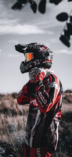 a man wearing a red and black motorcycle suit standing in front of some bushes with his helmet on