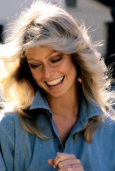 a woman smiling and looking down at her cell phone while she's wearing a denim shirt