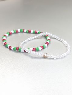 two beaded bracelets with red, green and white beads on a silver surface