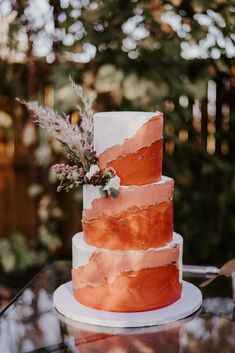 a three tiered wedding cake with pink and white frosting on a glass table