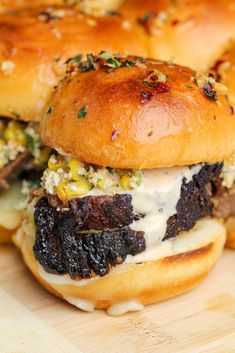 three sliders with meat and cheese on them sitting on a cutting board next to bread rolls