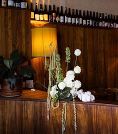 white flowers and greenery sit on a table in front of wine bottles at the bar