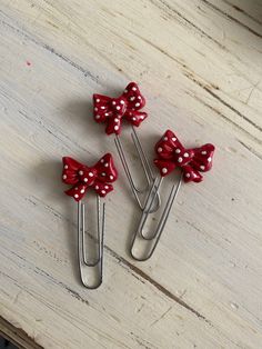 three red and white polka dot bow hair clips on a wooden table with scissors in the foreground