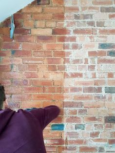 a man in purple shirt painting a brick wall