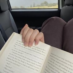 a person reading a book in the back seat of a car with their hands resting on an open book