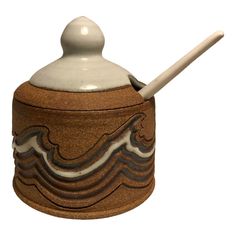 a brown and white ceramic container with a wooden spoon sticking out of it's lid