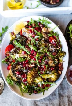 a white plate topped with broccoli and pomegranates next to other dishes