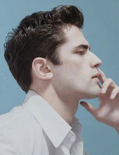 a man in a white shirt is holding his finger up to his nose and looking off into the distance