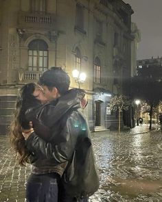 a man and woman kissing in the rain on a cobblestone street at night