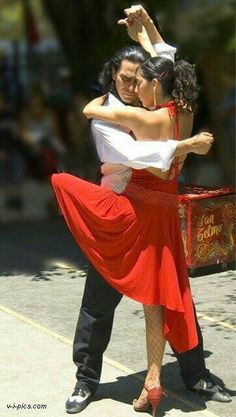 a man and woman dancing on the street with their arms around each other's shoulders