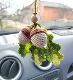 two crocheted acorns hanging from a car's dash board and steering wheel