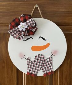 a snowman door hanger hanging from a wooden door with plaid fabric on it