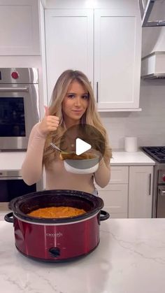 a woman holding a spoon in front of a slow cooker