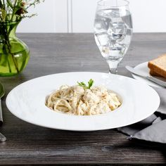 a white plate topped with pasta on top of a wooden table next to a glass of water