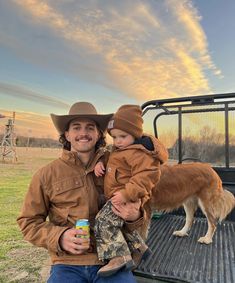 a man holding a small child in his arms while standing next to a dog on the back of a truck