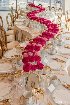 a long table is set up with pink flowers and gold place settings for an event