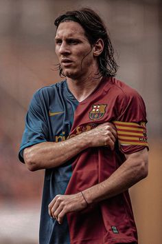 a man with long hair standing in front of a soccer ball and wearing a uniform