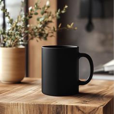 a black coffee mug sitting on top of a wooden table next to a potted plant