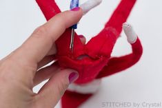 someone is sewing the bottom part of a red stuffed animal with scissors in their hand