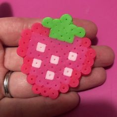 a hand holding a pink and green strawberry brooch on it's left side