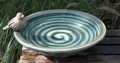 a small bird sitting on top of a green and white bowl next to some grass