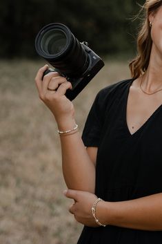 a woman holding a camera in her right hand and smiling at the camera with one eye open