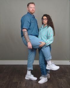 a man and woman are posing for a photo in front of a gray wall with their arms around each other