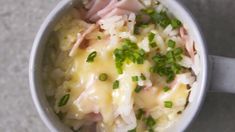 a cup filled with rice and ham on top of a gray countertop next to a spoon