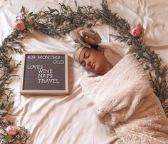 a woman laying in bed next to a book with flowers around her and a blanket over her head