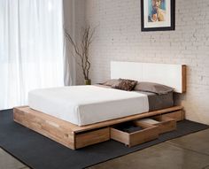 a bed with two drawers underneath it in a room next to a brick wall and window