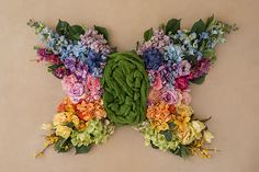 a butterfly made out of flowers and leaves on a wall in the shape of a rainbow