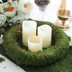 moss covered candle holders with white candles in the middle on a table next to flowers