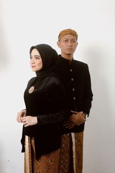 two people standing next to each other in front of a white wall wearing black clothing