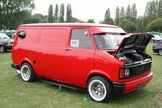 an old red van parked on top of a lush green field next to other cars