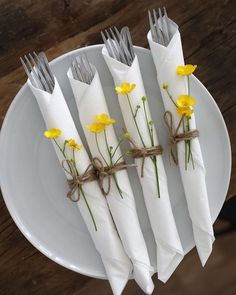 four napkins tied with twine and yellow flowers on a white plate next to silverware