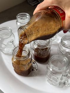 a person pouring something into some jars on a white plate with many glasses around it