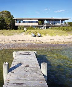 a wooden dock sitting in front of a house on top of a sandy beach next to the ocean