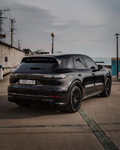 a black porsche cayen is parked on the side of the road by the ocean