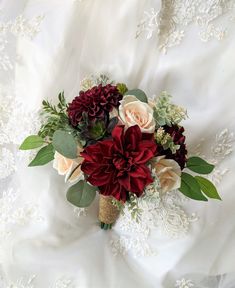 a bridal bouquet with red and white flowers is laying on a wedding dress sheet