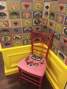 a red chair sitting in front of a wall covered with patches and pictures on it