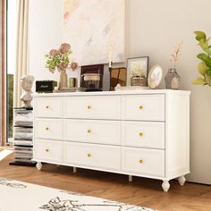 a white dresser sitting in a living room next to a large painting on the wall