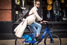 a woman riding on the back of a blue bike with a black bag in her hand