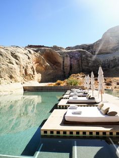 an outdoor swimming pool with lounge chairs and umbrellas in the sun near some mountains