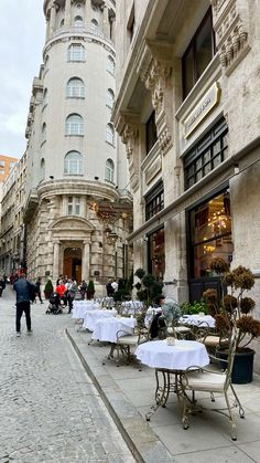 tables and chairs are set up on the sidewalk in front of an old stone building