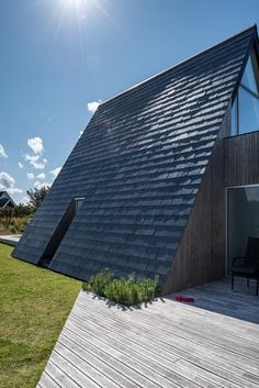 a house with a triangular roof and wooden decking on the outside, surrounded by grass