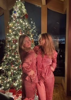 two women in pajamas standing next to a christmas tree