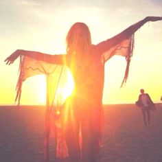 a woman standing on top of a beach next to the ocean with her arms outstretched